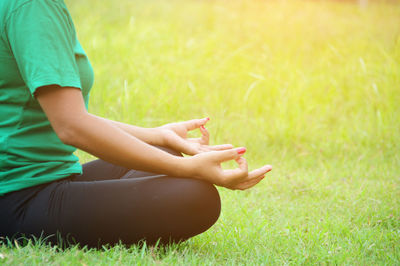 Midsection of woman practicing lotus position on grassy field