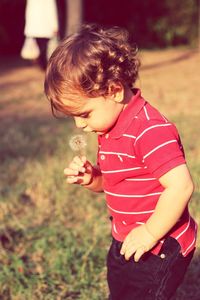 Side view of boy holding dandelion seed in back yard