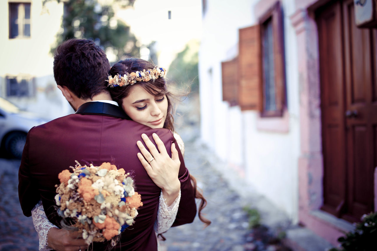 togetherness, focus on foreground, love, bonding, lifestyles, couple - relationship, leisure activity, building exterior, incidental people, young adult, young men, flower, arm around, casual clothing, person, bouquet, day
