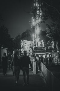 Rear view of people walking on illuminated street at night