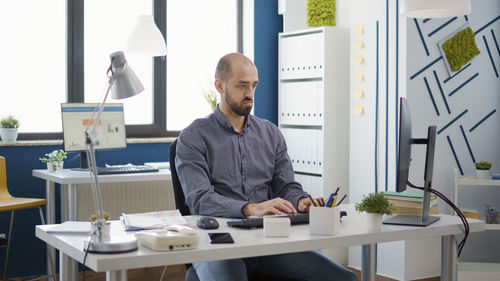 Young businessman using desktop pc sitting at desk in office