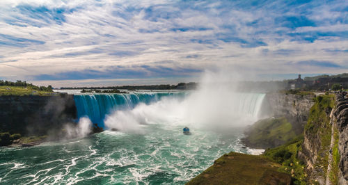 Scenic view of waterfall against cloudy sky