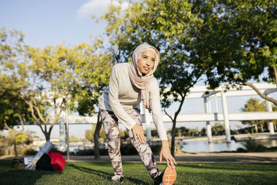 Pleasant arab female in hijab stretching legs while warming up before fitness training in park