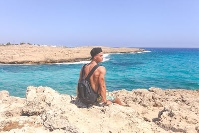 Rear view of shirtless man at beach against clear sky