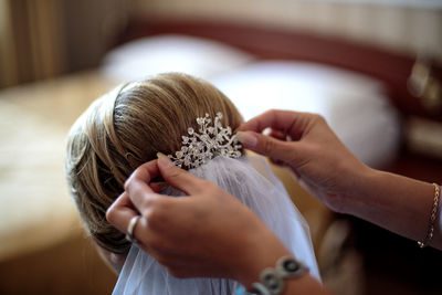 Cropped hands of beautician dressing bride at home