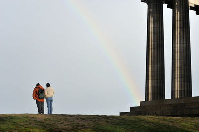 Rear view of people standing against rainbow in sky