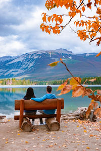 Rear view of man sitting on bench by lake against sky