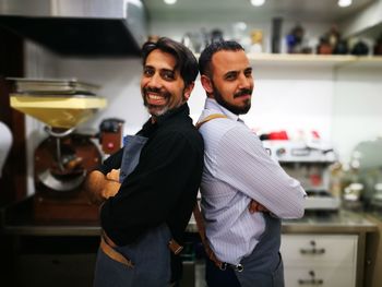 Portrait of smiling owners standing back to back in commercial kitchen