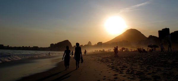 Silhouette people at beach against sky during sunset