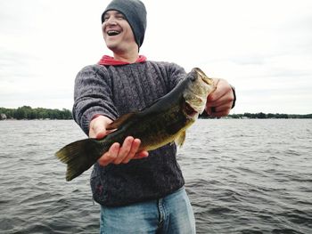 Man holding fish while standing against sea and sky