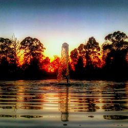 Silhouette trees by lake against clear sky during sunset