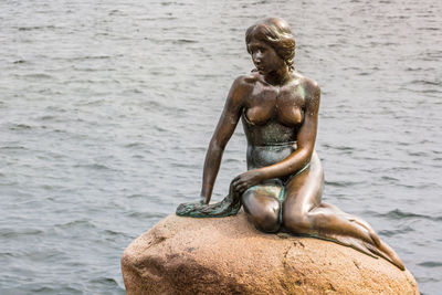 Statue of man on rock by sea