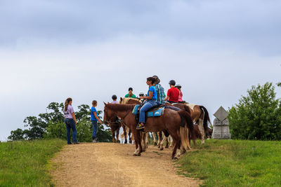 People riding horses on farm against sky