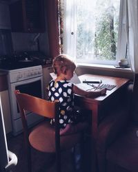 Rear view of girl studying at table by window