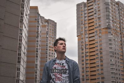 Low angle view of young man looking away against buildings in city