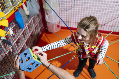 From above of little girl with angelman syndrome playing with development game while being fixed with elastic bands during therapy session with anonymous caregiver