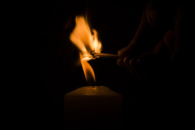 Cropped image of person igniting candle in darkroom