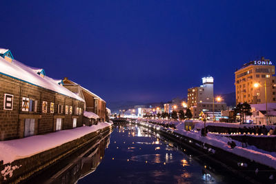 Illuminated residential district by canal against clear sky