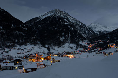 Snow covered houses by mountains against sky during winter