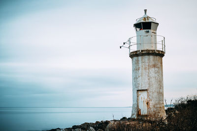 Lighthouse by sea against cloudy sky