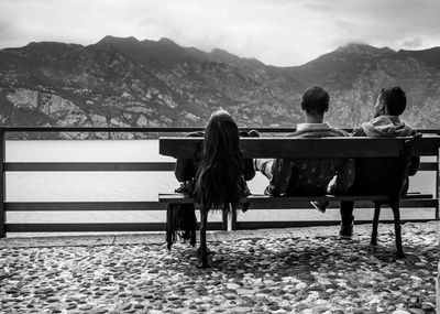 Rear view of friends sitting on bench at promenade against mountains