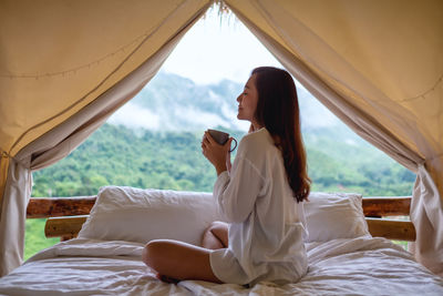 Portrait image of a beautiful young asian woman drinking coffee while sitting on a white bed