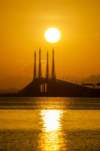 Silhouette built structure in sea against orange sky