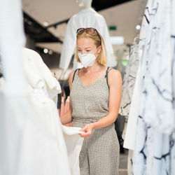 Mid adult woman wearing flu mask shopping at clothing store
