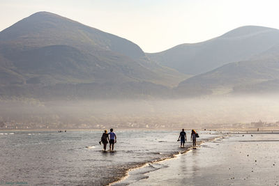 People walking at beach against mountains during sunny day