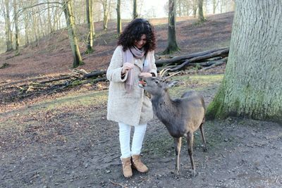 Woman feeding deer against trees at forest