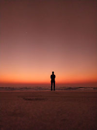 Silhouette man standing on beach against sky during sunset