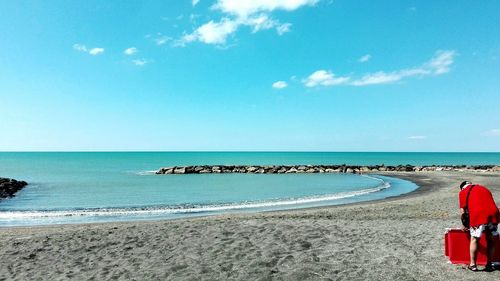 Rear view of man standing at beach against blue sky on sunny day