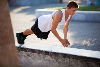 Full length of boy clapping during push-ups on retaining wall