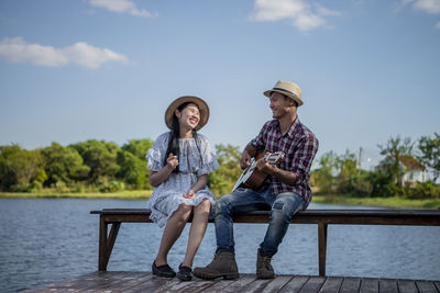 Full length of friends sitting on shore against sky