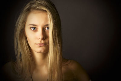 Portrait of young woman against black background