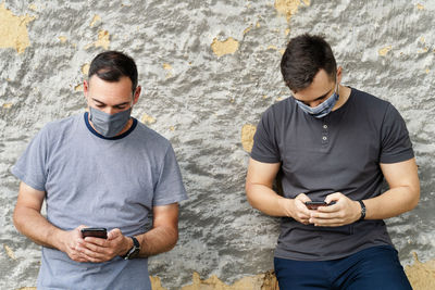 Full length of young man using mobile phone against wall