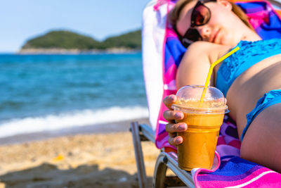 Woman holding drink while relaxing at beach