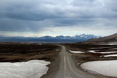 Road leading towards snowcapped mountains against sky