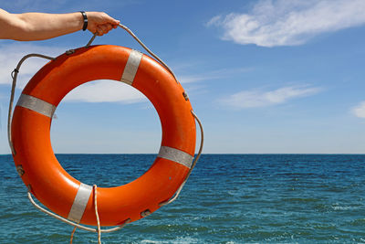 Close-up of hand holding life belt over sea against sky