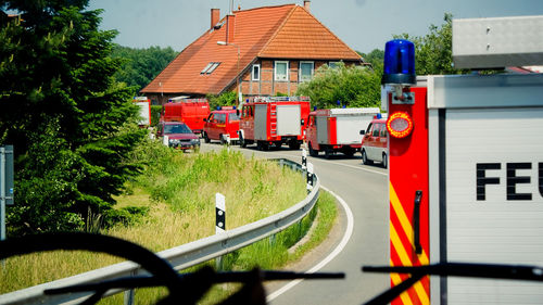 Road amidst trees and buildings with many cars of firefighters against sky
