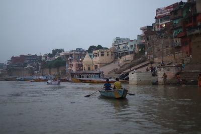 People on boat in river against buildings in city