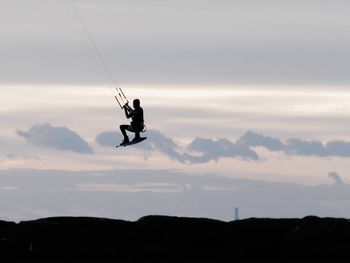 Silhouette person in mid-air against sky during sunset