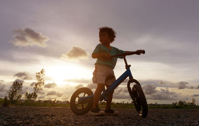 Boy on bicycle against cloudy sky at sunset