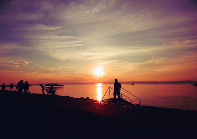 Silhouette people standing by lake against sky during sunset