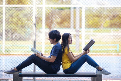 Couple of students are studying together, and a teenager sits on a seat beside court with a book.