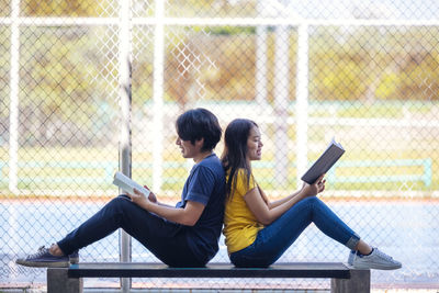 Full length of young woman using mobile phone while sitting outdoors