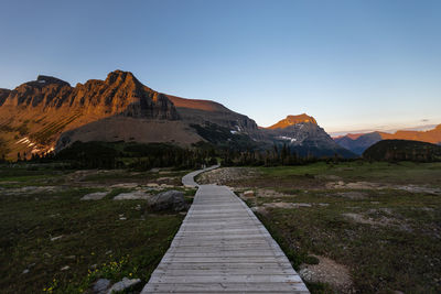 Footpath leading towards mountains against clear sky