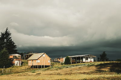 Stilt houses on field against cloudy sky