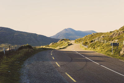 Road leading towards mountains against clear sky