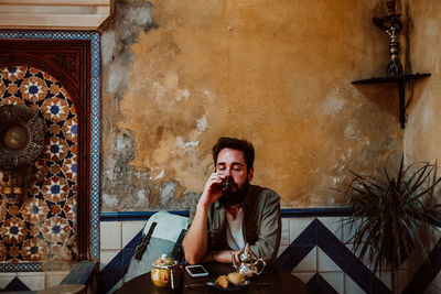 Portrait of young man using phone while sitting on table